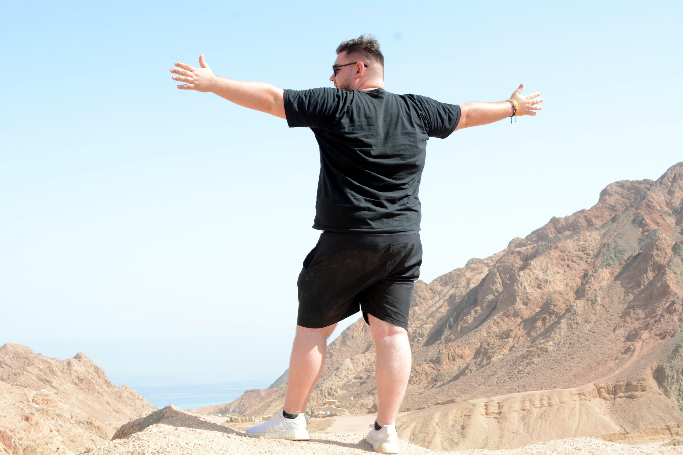 Alexander Brenner standing with arms spread wide against a desert mountain landscape